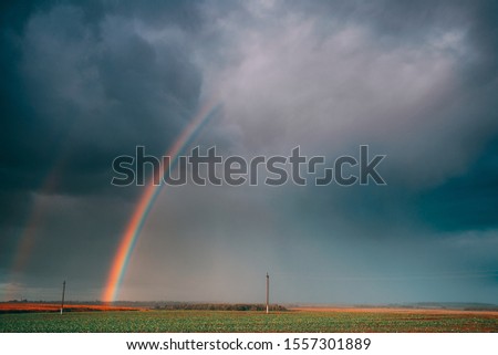 Dramatic Sky During Rain With Rainbow On Horizon Above Rural Landscape Field. Agricultural And Weather Forecast Concept. Countryside Meadow In Autumn Rainy Day.