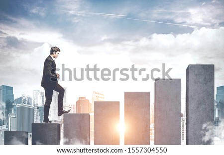 Confident young businessman climbing bar chart in modern city concept of business success and good career. Toned image Royalty-Free Stock Photo #1557304550