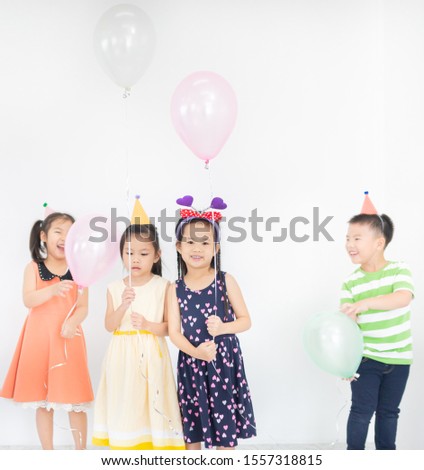 pretty asian children group standing and celebrate on gray background, they feeling happy in birthday party, they smile and play together, the holding Helium balloon, Christmas and new years party