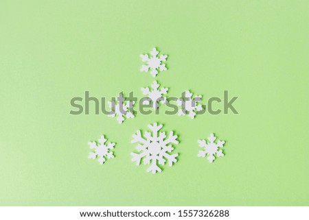 White wooden snowflakes on a light background. Snowflakes are laid out on a mint-colored background in the shape of a Christmas tree.