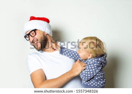 A young man in glasses and a Santa Claus hat plays with a child on a white background. Christmas concept, celebration with family, family holidays