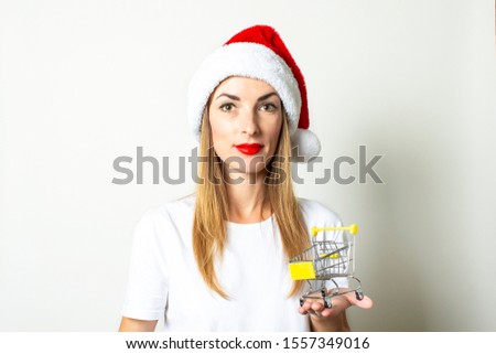 A young woman in a Santa Claus hat holds a shopping trolley in his hands on a white background. Christmas sale concept, black friday, discount