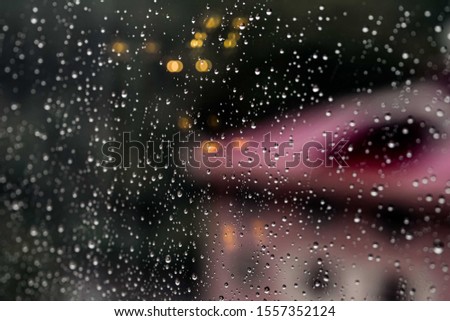 Drops of Rain On the glass with autumn city background. Warm Bokeh defocused Lights inside the house. Abstract Backdrop. Raindrops on a window glass.