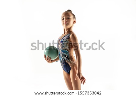 Little flexible girl isolated on white studio background. Little female model as a rhythmic gymnastics artist in bright leotard. Grace in motion, action and sport. Doing exercises with the ball.