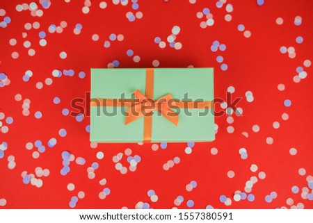 Festive Christmas and New Year background with green gift box, multicolored confetti on bright red background. Top View. Flat lay. Concept of preparation for holidays.