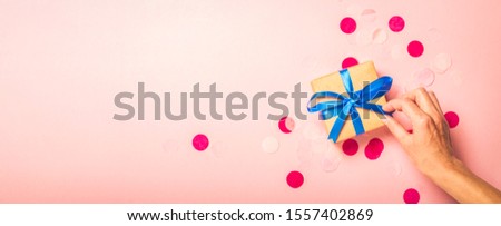 Female hand holds a gift on a pink background. Gift concept for a loved one, holiday, christmas. Banner. Flat lay, top view