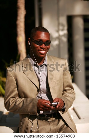 a well dressed african american business man text messages on his cell phone outside while listening on his personal digital music player