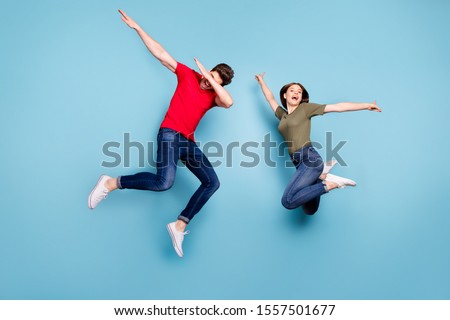 Full size photo of funky crazy two married people students  fun jump man perform dab dancers woman raise hands wear green red t-shirt denim jeans sneakers isolated blue color background Royalty-Free Stock Photo #1557501677