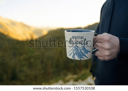 a man's hand holds a mug with the sign on the background of  the mountains on a sunny day