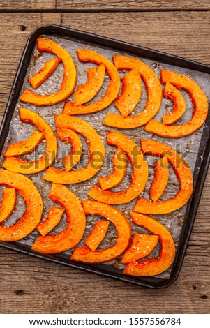 Baked pumpkin with vegetable oil, sesame seeds and spices. Vegan (vegetarian) healthy food concept. Metal pan on a wooden background, close up