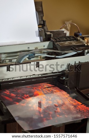 Old broken printer in workshop. The concept of cleaning and calibrating printers. Sunset and red sky with clouds in the photo. Picturesque nature photo printed on printing equipment.