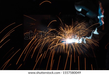 Welder in a factory. Bright blue and yellow sparks on a black background. Magical lig