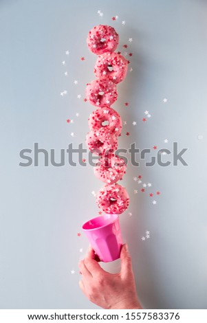 Creative image of perfect balance, tower or pyramid of tasty pink donuts balancing on bottom doughnut held by female hand. Popular hanukkah dessert. Conceptual equilibrium on light grey background.
