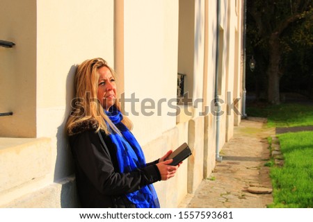 Nice portrait of a blonde woman, outside near a luxurious castle. Long-haired girl who smiles in the sun. Fashion model.