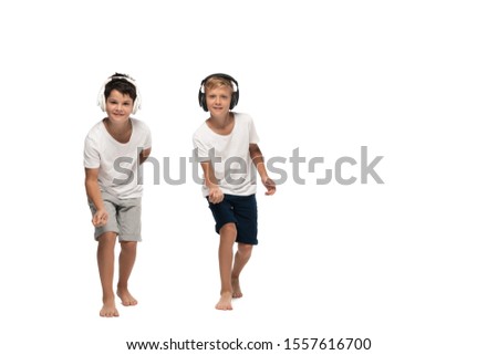 two brothers looking at camera and dancing while listening music in headphones on white background