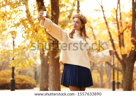 Stylish young woman taking selfie in autumn park