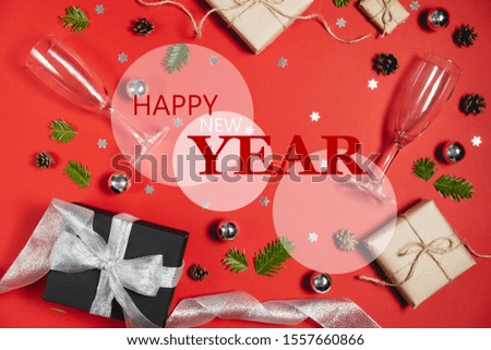 Happy New Year , Xmas bauble with handmade gift boxes decorated with craft paper of fir tree branches, two glasses champagne, pine and confetti on red background. Flat lay, top view, copy space