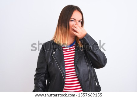 Young beautiful woman wearing striped shirt and jacket over isolated white background smelling something stinky and disgusting, intolerable smell, holding breath with fingers on nose. Bad smells
