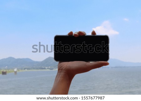 Woman hand holding mobile phone blank black screen, background of mountain and lagoon.