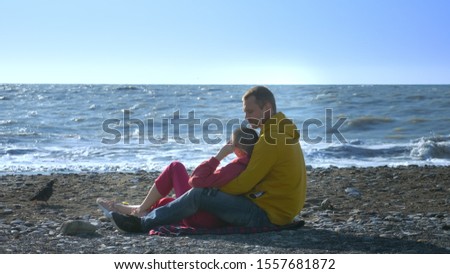couple in love man and a bald woman are sitting on the seashore in cool windy weather.