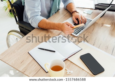 Cropped view of man in wheelchair holding credit card and using laptop