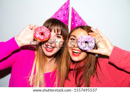 Portrait of two hungry young asian women holding two donuts isolated over  grey background.Picture of amazing two women friends eating donuts isolated over pink background. Looking camera