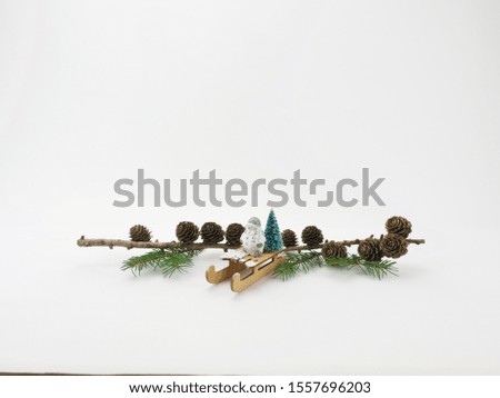 Snowman on a sled, behind him a branch with cones and green branches of a Christmas tree, ecological concept, white background, front picture