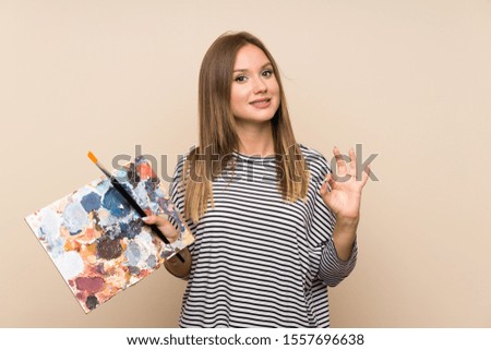 Teenager girl holding a palette over isolated background showing an ok sign with fingers
