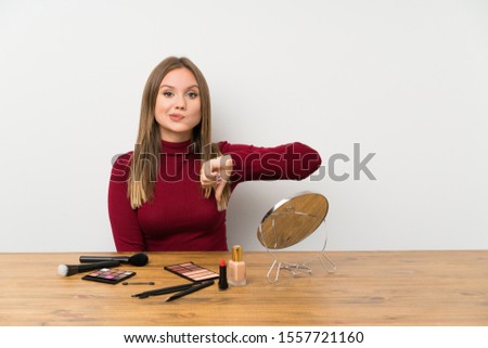 Teenager girl with makeup palette and cosmetics in a table showing thumb down sign