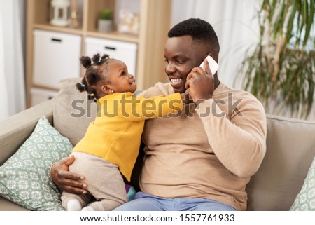 family, fatherhood and technology concept - happy african american father with baby at home calling on smartphone