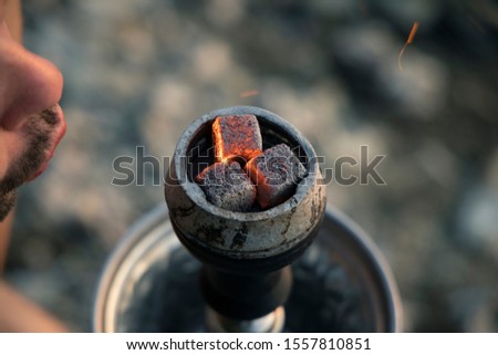 blowing hookah coals and sparkles by man lips preparing for relaxing smoking process, blurred background empty space for your copy or text here