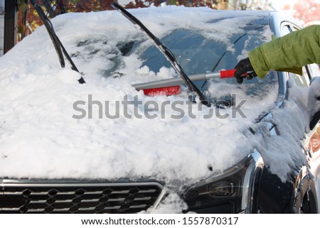 winter safety - a person cleaning the snow from the windshield of a car Royalty-Free Stock Photo #1557870317