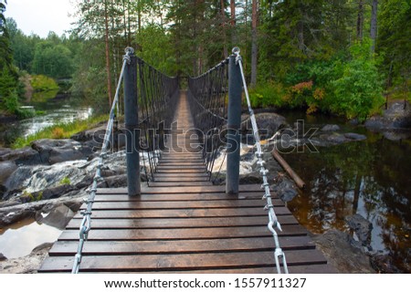 Suspension cable bridge crossing the river, ferriage in the woods Royalty-Free Stock Photo #1557911327