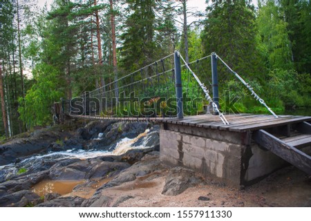 Suspension cable bridge crossing the river, ferriage in the woods Royalty-Free Stock Photo #1557911330
