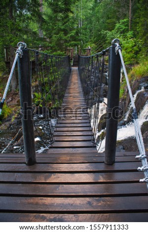 Suspension cable bridge crossing the river, ferriage in the woods Royalty-Free Stock Photo #1557911333