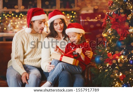 Adorable little festive girl openng xmas gifts on Christmas eve with mom and dad, decorated kitchen interior, copy space