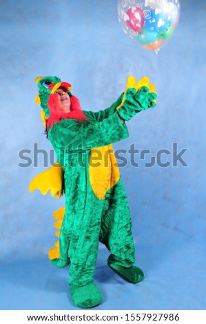Animator in a green dragon costume with a yellow belly with a ball in the Studio on a blue background