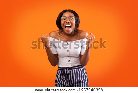 Yes. Excited Afro Lady Shouting Shaking Fists Celebrating Success Standing Over Orange Background. Studio Shot Royalty-Free Stock Photo #1557940358