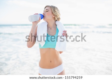 Relaxed blonde woman in sportswear drinking water on the beach
