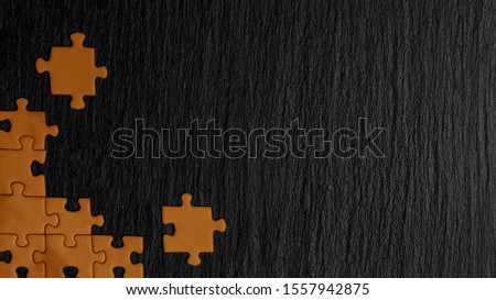Orange puzzle in the corner of the image on a black natural stone background of slate. A frame with an empty space for your description. Royalty-Free Stock Photo #1557942875