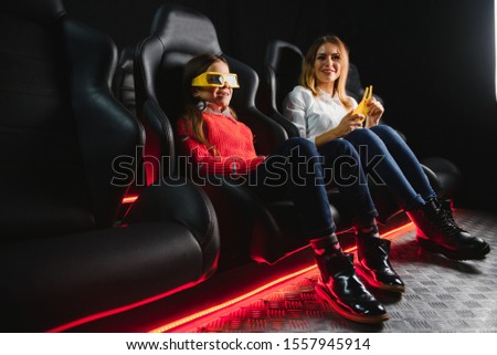 Happy mother and daughter wearing 3d glasses in cinema. Cheerful family watching funny film and enjoying spare time together in movie house. Concept of enjoyment and fun.