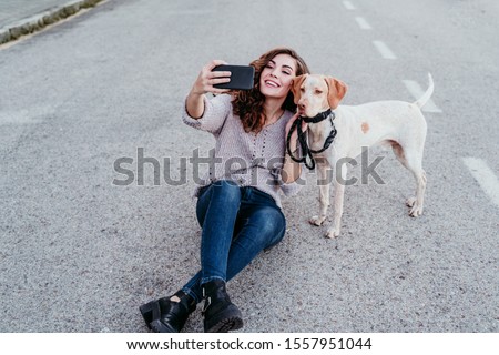 young woman taking a selfie with mobile phone with her dog at the street. autumn season