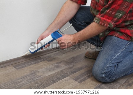 Construction worker caulking  batten of laminate floor using silicone glue in a cartridge, home renovation Royalty-Free Stock Photo #1557971216