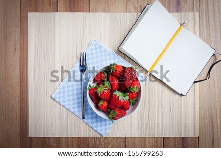Bowl of fresh strawberries with white recipe book