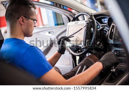Automobile computer diagnosis. Car mechanic repairer looks for engine failure on diagnostics equipment in vehicle service workshop Royalty-Free Stock Photo #1557995834