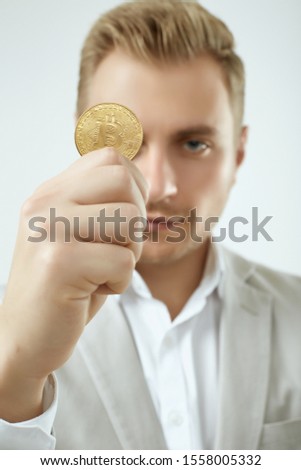 Portrait of a handsome blonde man model in a fashion gray suit holds a Bitcoin isolated on white background in studio