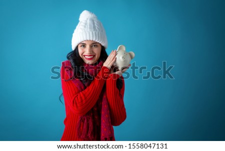 Young woman in winter clothes with a piggy bank on a dark blue background