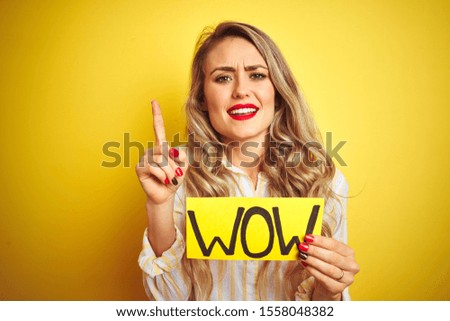 Beautiful woman holding amazed wow surprise banner over isolated yellow background surprised with an idea or question pointing finger with happy face, number one