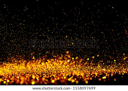 Sparkling gold glitter powder on black background.
Bokeh orange and Yellow diamond silver sparkle glitter for texture background.
Sprinkle dust golden light Christmas and  happy new year. 