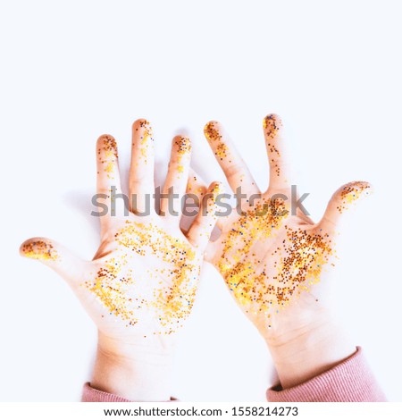 Little child with gold glitter on hands against white background, top view. Overhead shot of girl hands with sparkly golden confetti on white background. Christmas party, New Year celebration